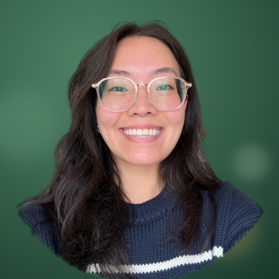 Portrait of Victoria Day, smiling, with long dark hair and glasses, wearing a navy knit sweater